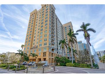 Upscale condo building with tropical landscaping, fountain, and luxury entrance, under a blue sky with wispy clouds at 750 N Tamiami Trl # 814, Sarasota, FL 34236