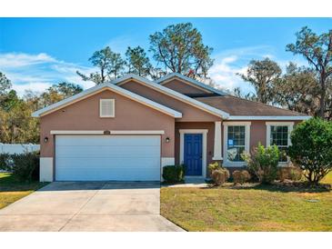 Tan one-story house with white garage door and blue front door, surrounded by green lawn at 2729 Walden Woods Dr, Plant City, FL 33566
