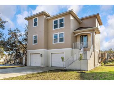 Two-story home with tan stucco, white trim, garage, and front stairs with white railing at 7327 Brightwaters Ct, New Port Richey, FL 34652