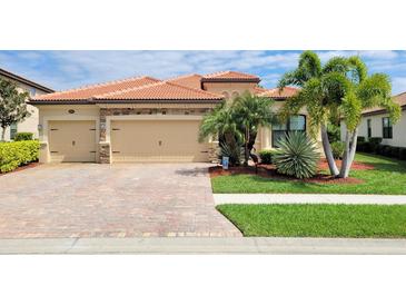 Tan house with three-car garage, paver driveway and lush landscaping at 20590 Granlago Dr, Venice, FL 34293