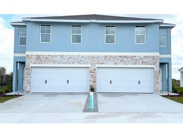 Two-story duplex with light blue exterior, two-car garage, and stone accents at 13992 Emerald Fields Dr, Hudson, FL 34667