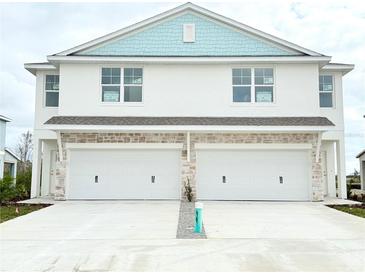 Two-story duplex with light blue accents, two-car garage, and driveway at 14024 Emerald Fields Dr, Hudson, FL 34667