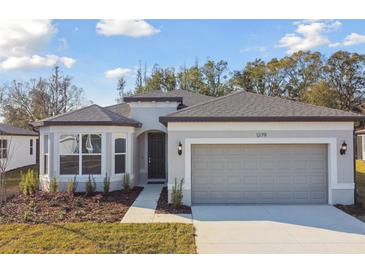 Single-story home with gray siding, two-car garage, and landscaping at 1279 Kazaz Ct, Zephyrhills, FL 33540