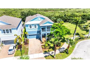 Two-story light blue house with paver driveway, landscaping, and a view of a nature preserve at 905 Seagrape Dr, Ruskin, FL 33570