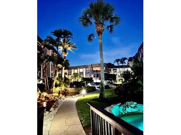 Night view of condo building with lush landscaping, walkways, and a pond at 3035 Countryside Blvd # 14B, Clearwater, FL 33761