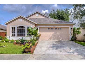 Tan one-story house with a two-car garage and landscaped front yard at 10922 Brucehaven Dr, Riverview, FL 33578