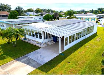 Mobile home with large sunroom and carport, situated on a spacious lot with lush lawn at 15 Hamilton Ln # 7, Palm Harbor, FL 34684