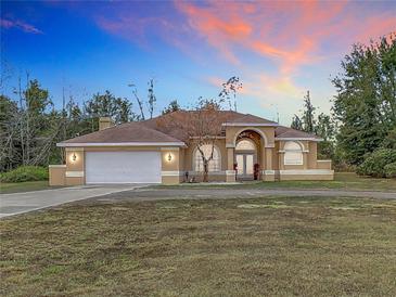 House exterior featuring a tan stucco exterior, large windows, and a three-car garage at 4367 Burns Rd, Brooksville, FL 34602