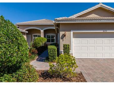 Charming front exterior showcasing a two-car garage, brick driveway, and meticulously landscaped walkway at 16233 Amethyst Key Dr, Wimauma, FL 33598