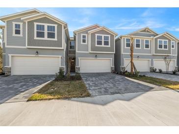 Three-story townhouses with gray siding, white garage doors, and gray paver driveways at 31496 Woodland Race Loop, Wesley Chapel, FL 33545
