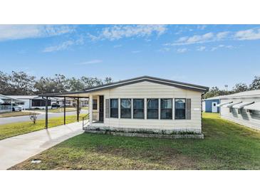 Tan mobile home with carport and landscaped lawn at 35934 Verano Ln, Zephyrhills, FL 33541