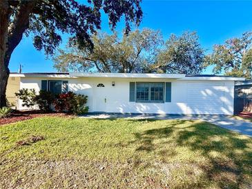 Newly renovated house with a white exterior, green lawn, and driveway at 1833 Knollwood Dr, Holiday, FL 34690