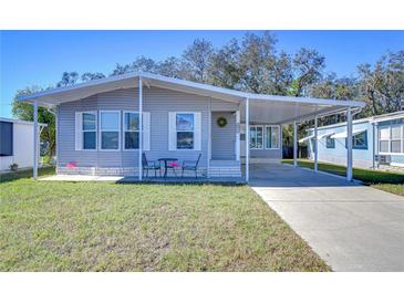 Gray mobile home with carport, landscaped lawn, and seating area at 4853 Blanco Dr, Zephyrhills, FL 33541