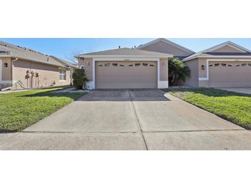 Front view of a beige house with a two-car garage and grassy area at 31447 Shaker Cir, Wesley Chapel, FL 33543
