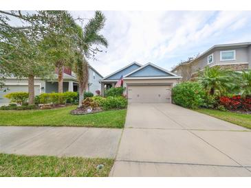 Tan house with blue accents, two-car garage, and landscaped yard at 6516 Salt Creek Ave, Apollo Beach, FL 33572