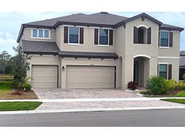 Two-story house with beige exterior, dark brown accents, and a three-car garage at 12854 Boggy Creek Dr, Riverview, FL 33579