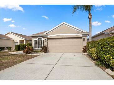 Tan house with two-car garage, landscaping, and palm tree at 2749 Plantain Dr, Holiday, FL 34691