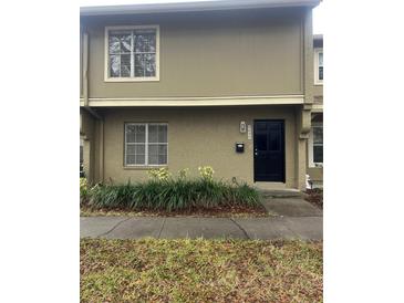 Tan two-story townhome with black door, landscaping, and sidewalk at 7638 Woodbridge Blvd, Tampa, FL 33615