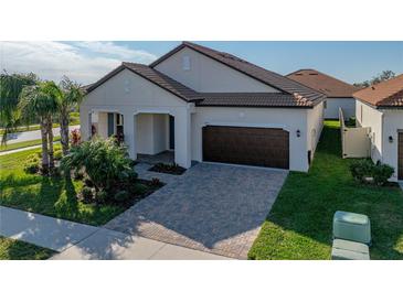 Single-story home with a brown door and brick driveway, featuring landscaping and a two-car garage at 16931 Scuba Crest St, Wimauma, FL 33598