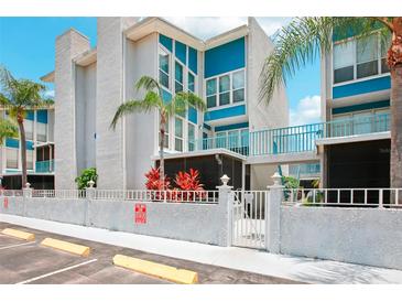 Condo building exterior, featuring a teal and white color scheme, gated entrance, and tropical landscaping at 343 Rex Pl # F, Madeira Beach, FL 33708