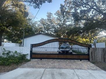 Attractive home with a wood and metal gate, paved driveway, and mature landscaping at 3005 E 148Th Ave, Lutz, FL 33559
