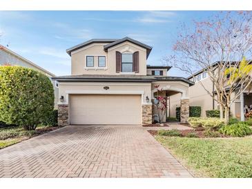 Two-story house with beige exterior, brick driveway, and landscaping at 18811 Deer Tracks Loop, Lutz, FL 33558