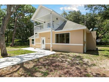 Tan two-story house with white trim, balcony, and a walkway at 7803 Cadillac Ave, Hudson, FL 34667