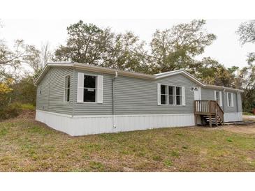 Gray manufactured home with white skirting, wooden steps, and surrounding trees at 12816 Midvale Ave, New Port Richey, FL 34654