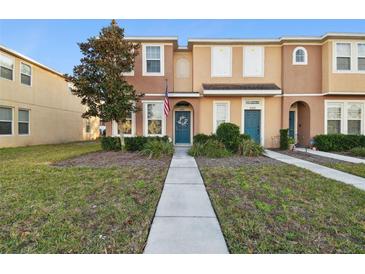 Tan two-story townhome with teal door, American flag, and landscaped lawn at 8841 Walnut Gable Ct, Riverview, FL 33578
