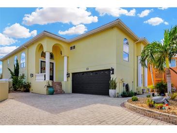 Two-story yellow home featuring a brick driveway, arched entryway and a black two car garage door at 808 Symphony Isles Blvd, Apollo Beach, FL 33572