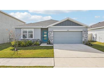 One-story home with gray siding, teal door, and landscaped lawn at 31814 Oyster Trellis Ln, Wesley Chapel, FL 33545