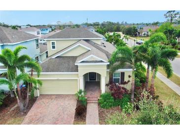 Two-story house with a light beige exterior, brick driveway, and lush landscaping at 5230 Admiral Pointe Dr, Apollo Beach, FL 33572