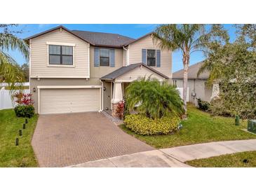 Two-story house with a tan exterior, brick driveway, and lush landscaping at 13355 Orca Sound Dr, Riverview, FL 33579