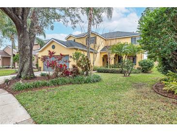 Two-story yellow house with gray garage door and lush landscaping on a spacious lot at 5608 Rockfield Loop, Valrico, FL 33596