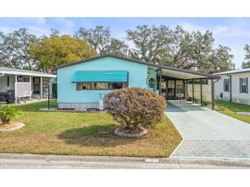 Light teal single-wide manufactured home with carport and landscaped yard at 4822 Sedeno Dr, Zephyrhills, FL 33541