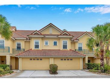 Tan three-story townhome with two-car garage, and lush landscaping at 2648 Tanglewood Trl, Palm Harbor, FL 34685