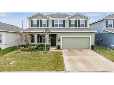 Two-story house with green exterior, two-car garage, and landscaped lawn at 7878 Greenway Ave, Wesley Chapel, FL 33544