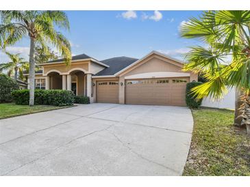 Tan house with three-car garage, landscaping, and palm trees at 9232 Brindlewood Dr, Odessa, FL 33556