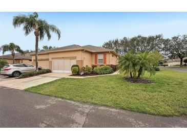 Tan single-story home with attached garage, landscaping, and palm trees at 2028 Acadia Greens Dr, Sun City Center, FL 33573