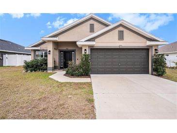 Beige house with dark gray garage door, landscaping, and a walkway at 11521 Sunder Berry St, Hudson, FL 34667