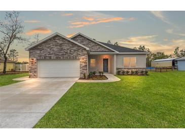 House exterior featuring stone accents, a two-car garage, and a well-manicured lawn at 15171 Pomp Parkway, Weeki Wachee, FL 34614