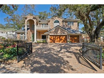 Stately brick home with a two-car garage, balcony, mature trees and an ornate front gate at 4407 W Dale Ave, Tampa, FL 33609
