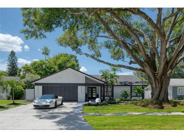 Modern mid-century home with white brick exterior, dark gray garage door, and manicured landscaping at 14040 Cascade Ln, Tampa, FL 33618
