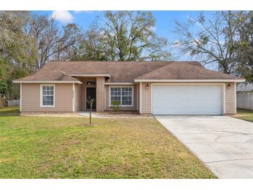 Beige house with brown roof, white garage door, and landscaped lawn at 5332 Nutcracker Cir, Land O Lakes, FL 34639
