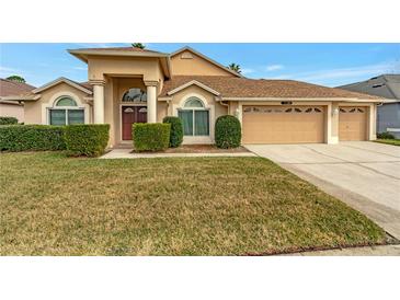 Tan house with three-car garage, lush lawn, and manicured hedges at 10025 Cypress Shadow Ave, Tampa, FL 33647