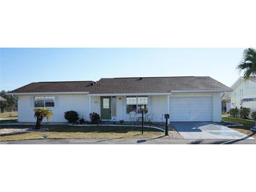White single-story home with a green door, attached garage, and well-manicured lawn at 711 E Brockton Pl, Sun City Center, FL 33573