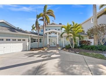 Stunning waterfront home with a light teal exterior, palm trees, and a two-car garage at 17077 Dolphin Dr, North Redington Beach, FL 33708