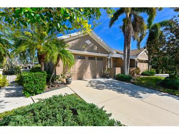 Tan house with two-car garage, lush landscaping, and a paved driveway at 7402 Hamilton Rd, Bradenton, FL 34209