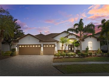 Beautiful home featuring a three-car garage, lush landscaping, and a paver driveway at 1893 Riveredge Dr, Tarpon Springs, FL 34689