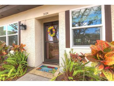 Charming front door with a colorful welcome mat, vibrant wreath, and beautiful landscaping at 3124 Highlands Blvd, Palm Harbor, FL 34684